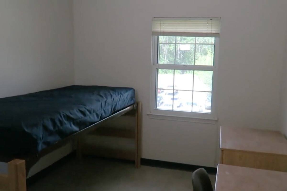 Sparsely furnished dorm room with a window on the wall between a single bed and desk.