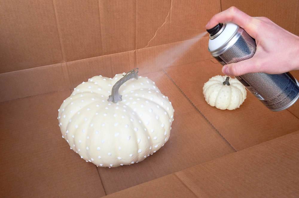 A person is spraying a pumpkin a white color.