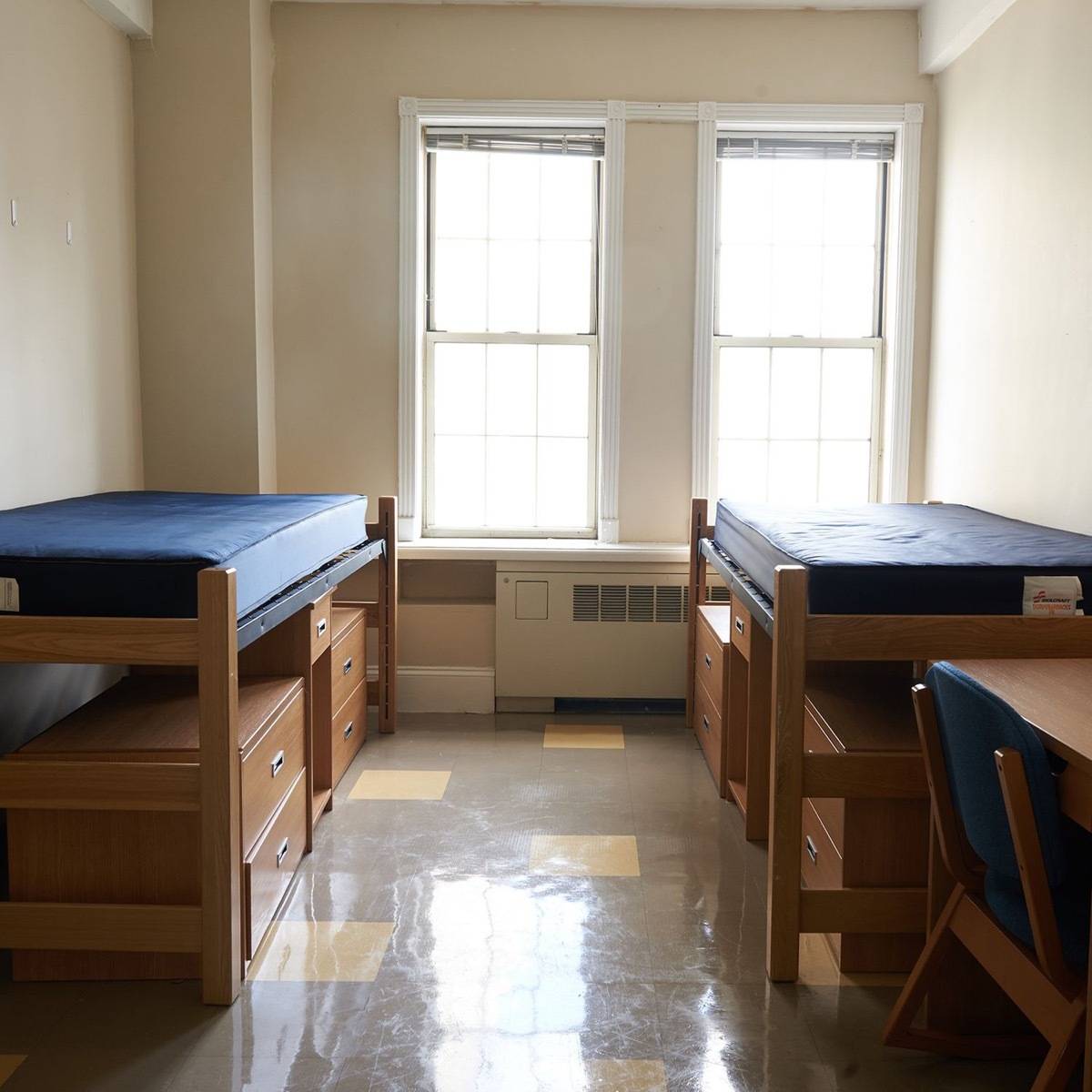 Beds sit across from each other in a semi-empty dorm room.