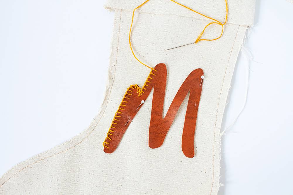 A white stocking with a leather M stitched to it.