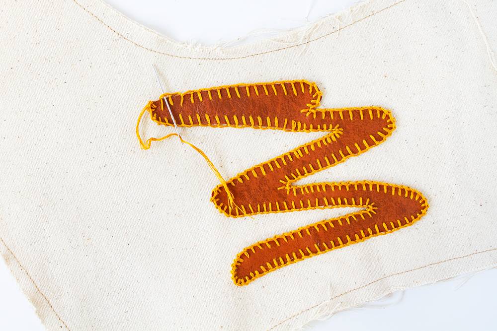 A brown squiggly design that has been stitched onto a white t-shirt with yellow stitching.