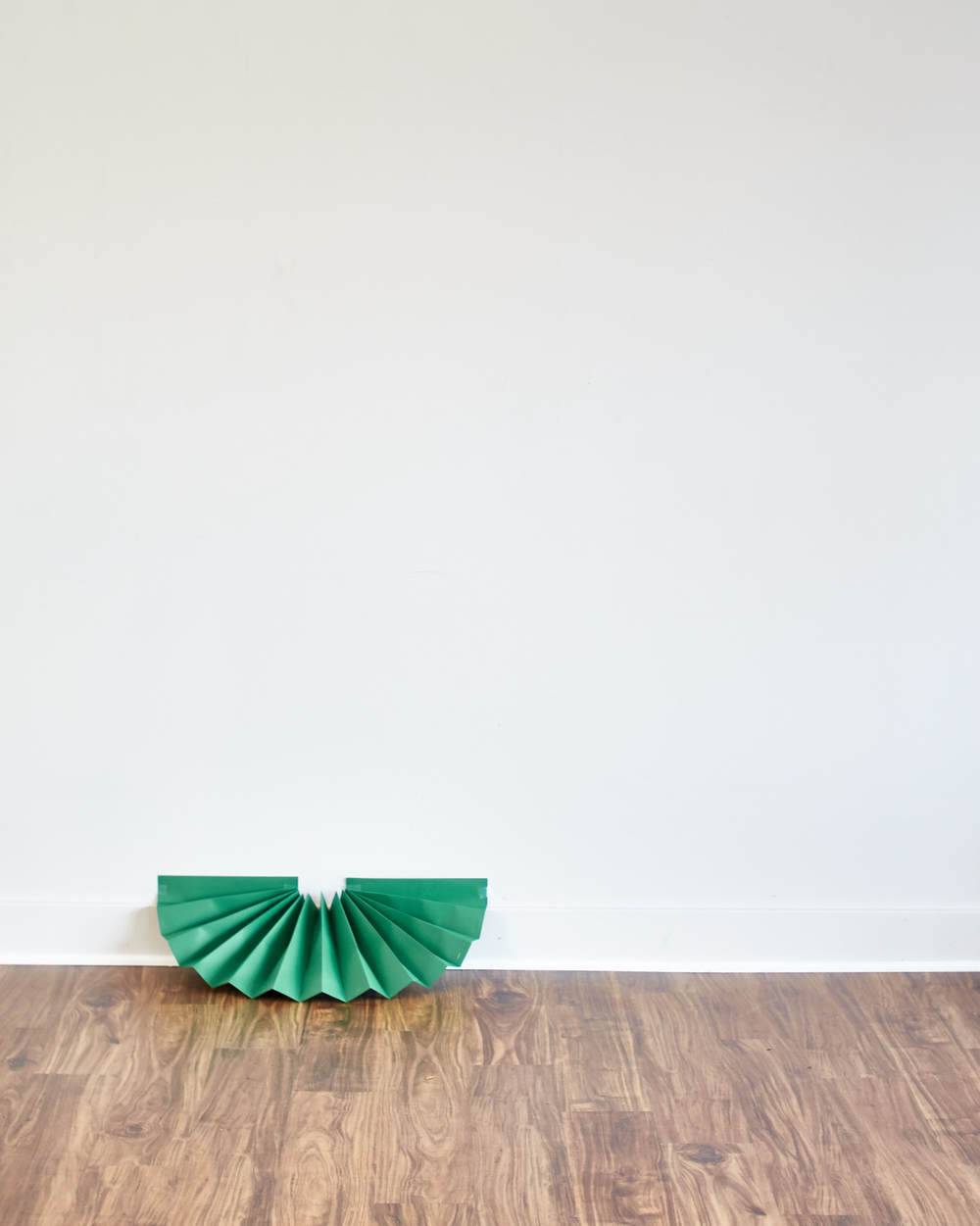 A green fan is sitting on the floor near a white wall.