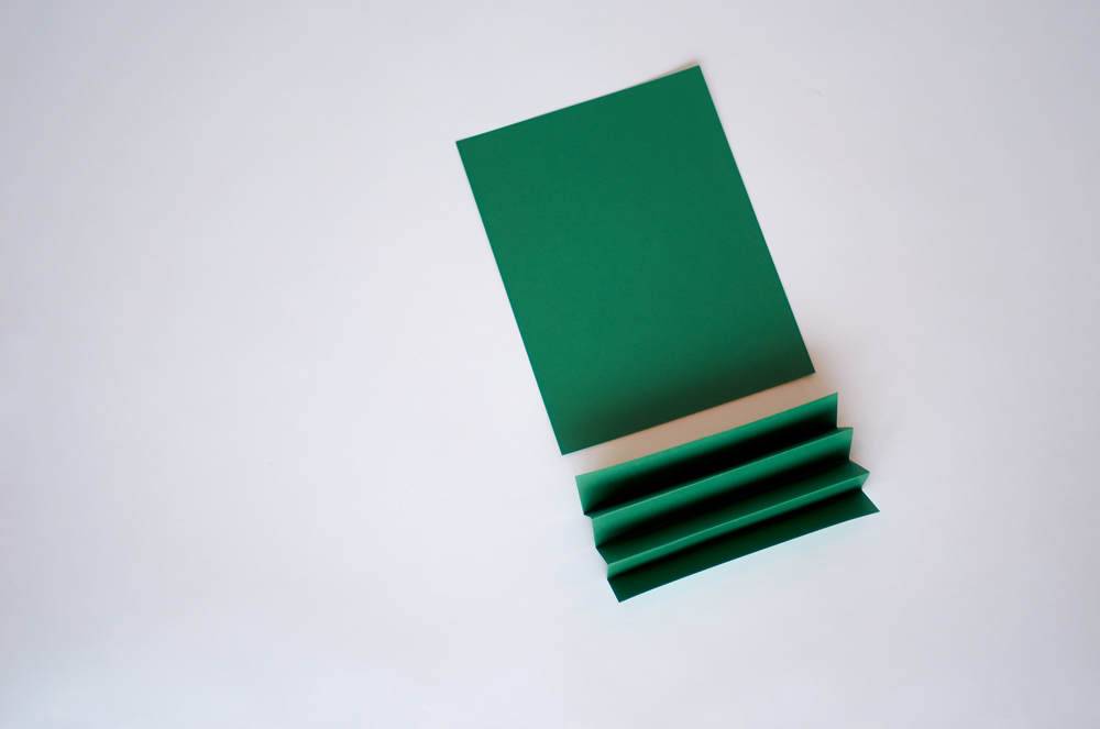 A rectangular piece of green paper next to a three times folded piece of green paper.