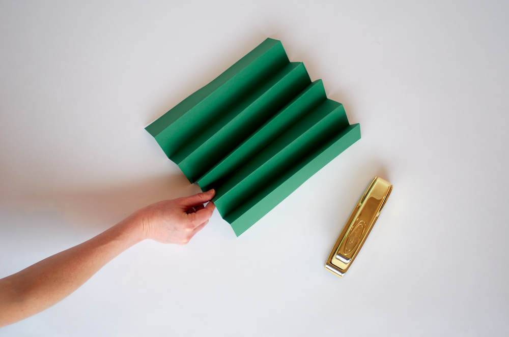 A person's arm holds a green origami folding next to a brass object.