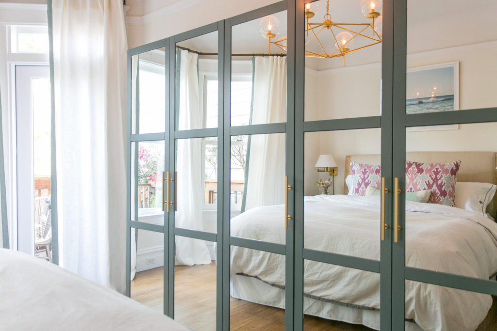 A bed with white bedding is reflected in a wall of mirrors.