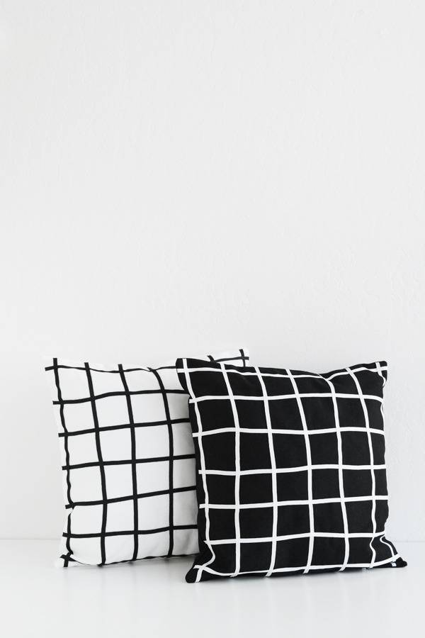 A white pillow with black vertical and horizontal stripes and a black pillow with white vertical and horizontal stripes.
