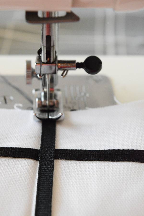 A sewing machine sewing a black strip onto a piece of white cloth.