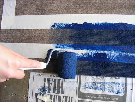 A hand is shown painting a surface blue with a paint sponge.