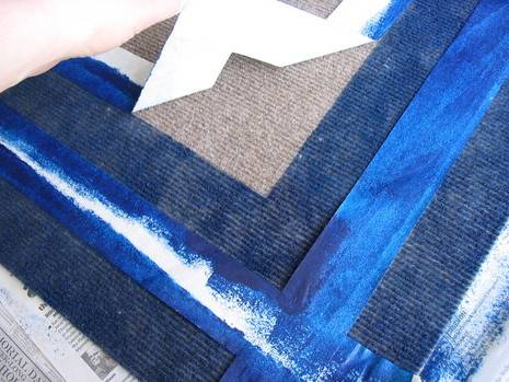 Tape is being peeled away from a rug with blue paint.