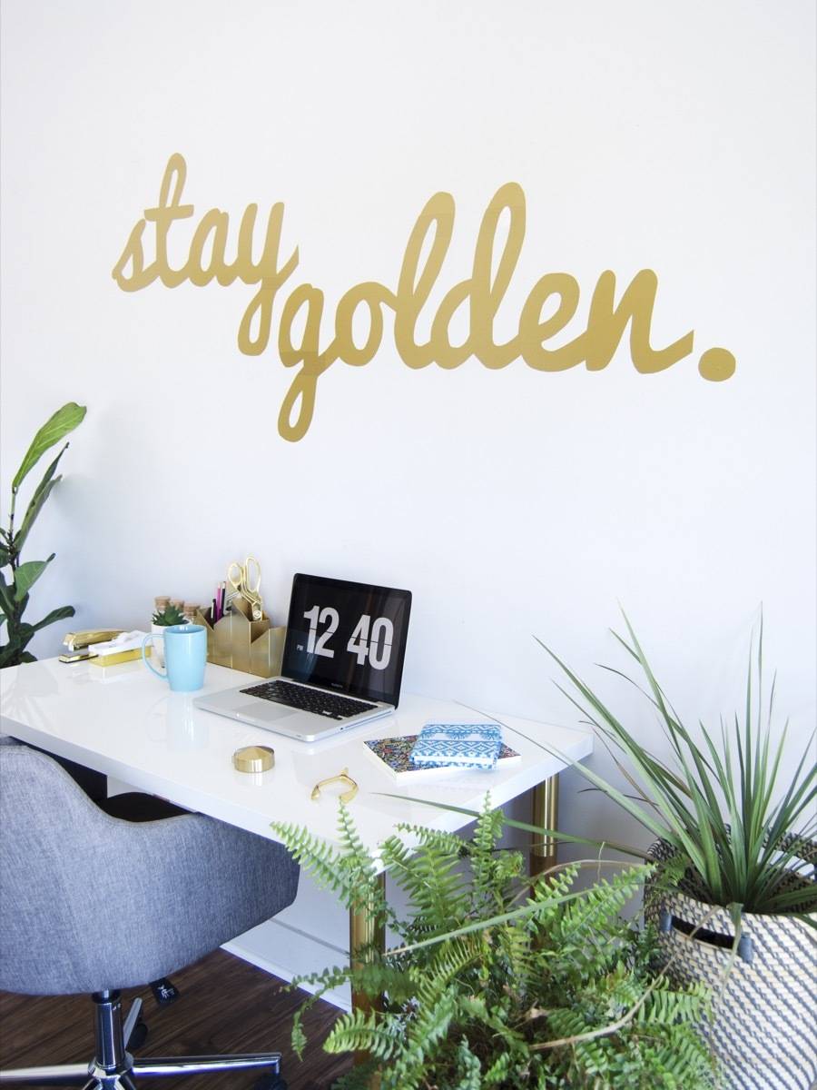 Desk and a chair sitting under a "stay golden" sign painted on the wall.