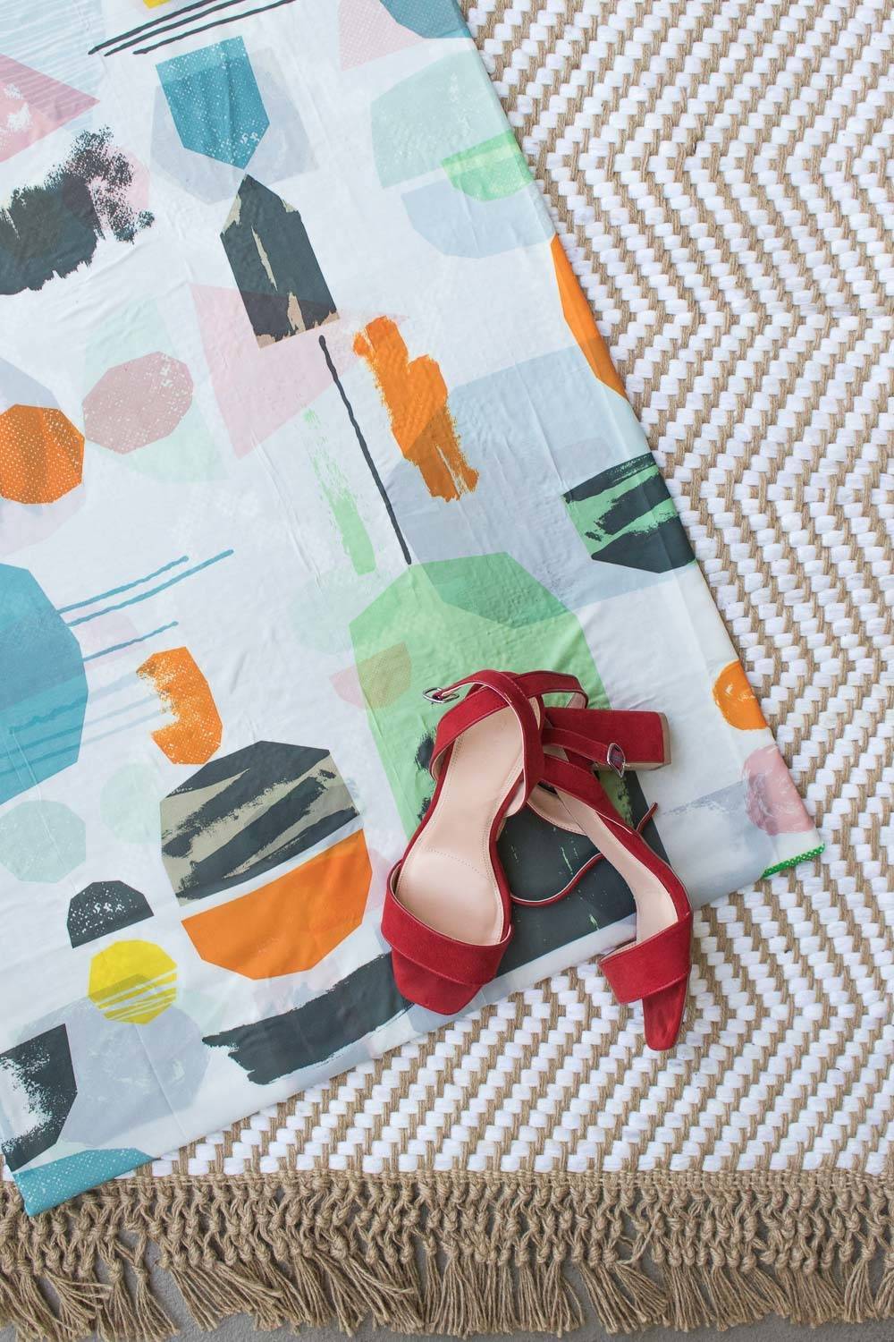 Red shoes sit on a colorful blanket.