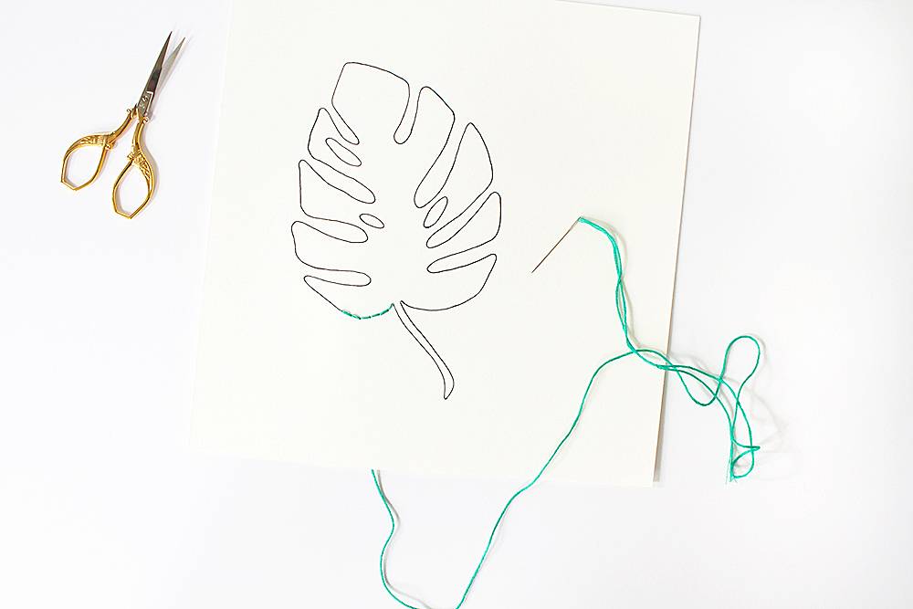 Doing embroidery on leaf art and a scissor is near by.