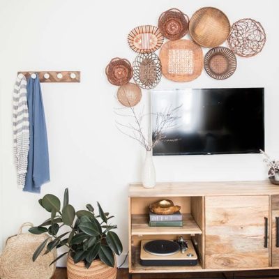 An area is decorated with low piece of furniture under a flat screen tv mounted on the wall with assorted baskets flanking the television and a coat hook hanging beside it.