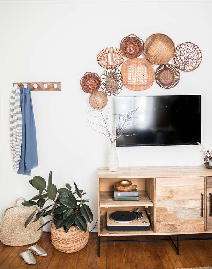 An area is decorated with low piece of furniture under a flat screen tv mounted on the wall with assorted baskets flanking the television and a coat hook hanging beside it.