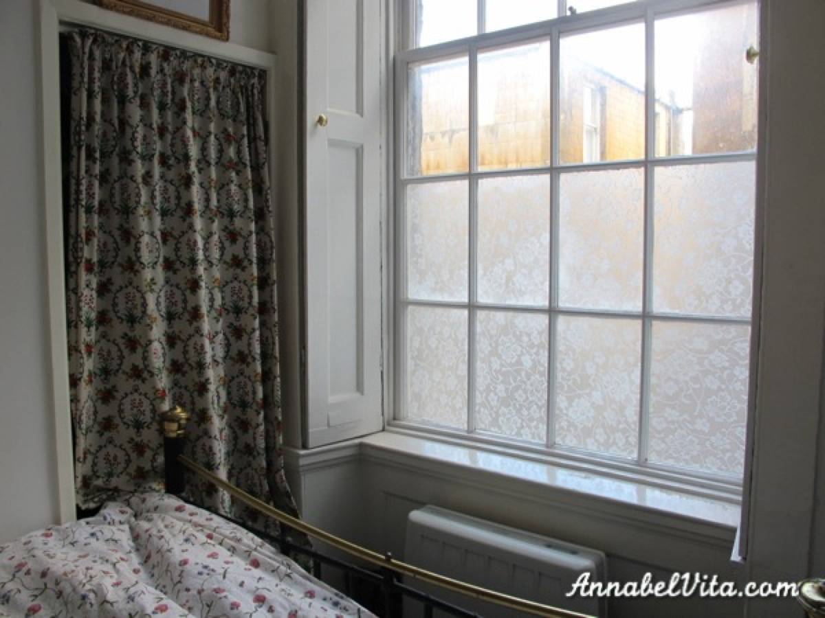 A brass bed frame facing a window with the bottom half frosted.