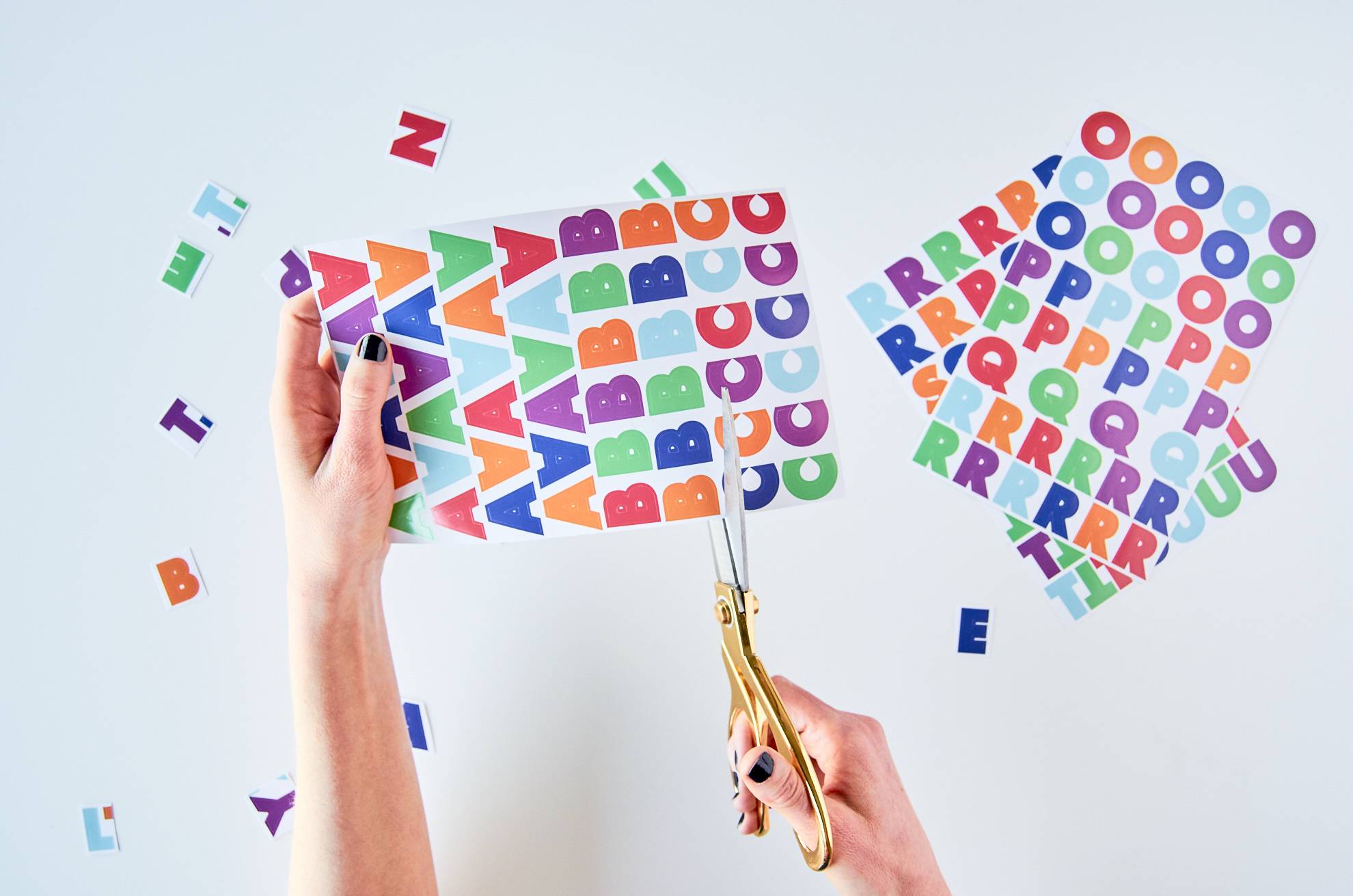 A woman cuts out colorful letters from a sheet of stickers.