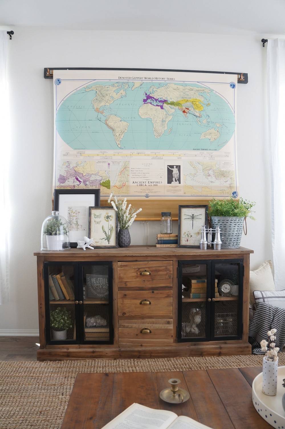 A full rustic bookshelf with drawers in the middle and picture frames on top sits under a world map.