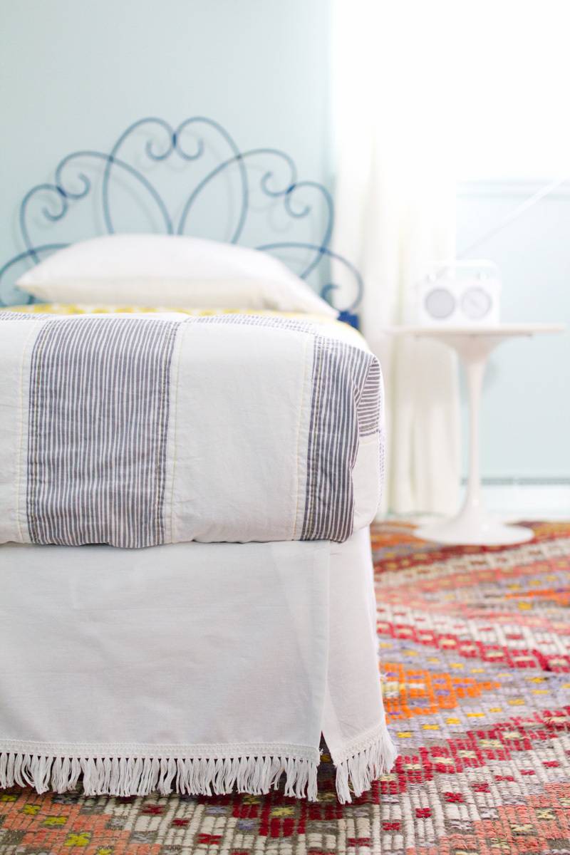 Bed with scroll headboard and white bedding set on a multicolored rug featuring diamond pattern.