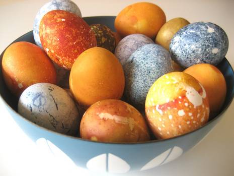 Orange, yellow, blue and white eggs are in a blue and white bowl.