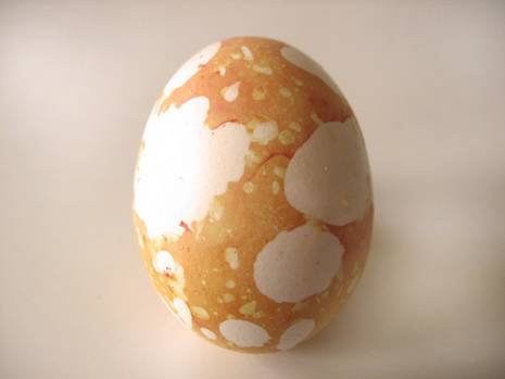 An egg sitting on a white surface is yellow and white.