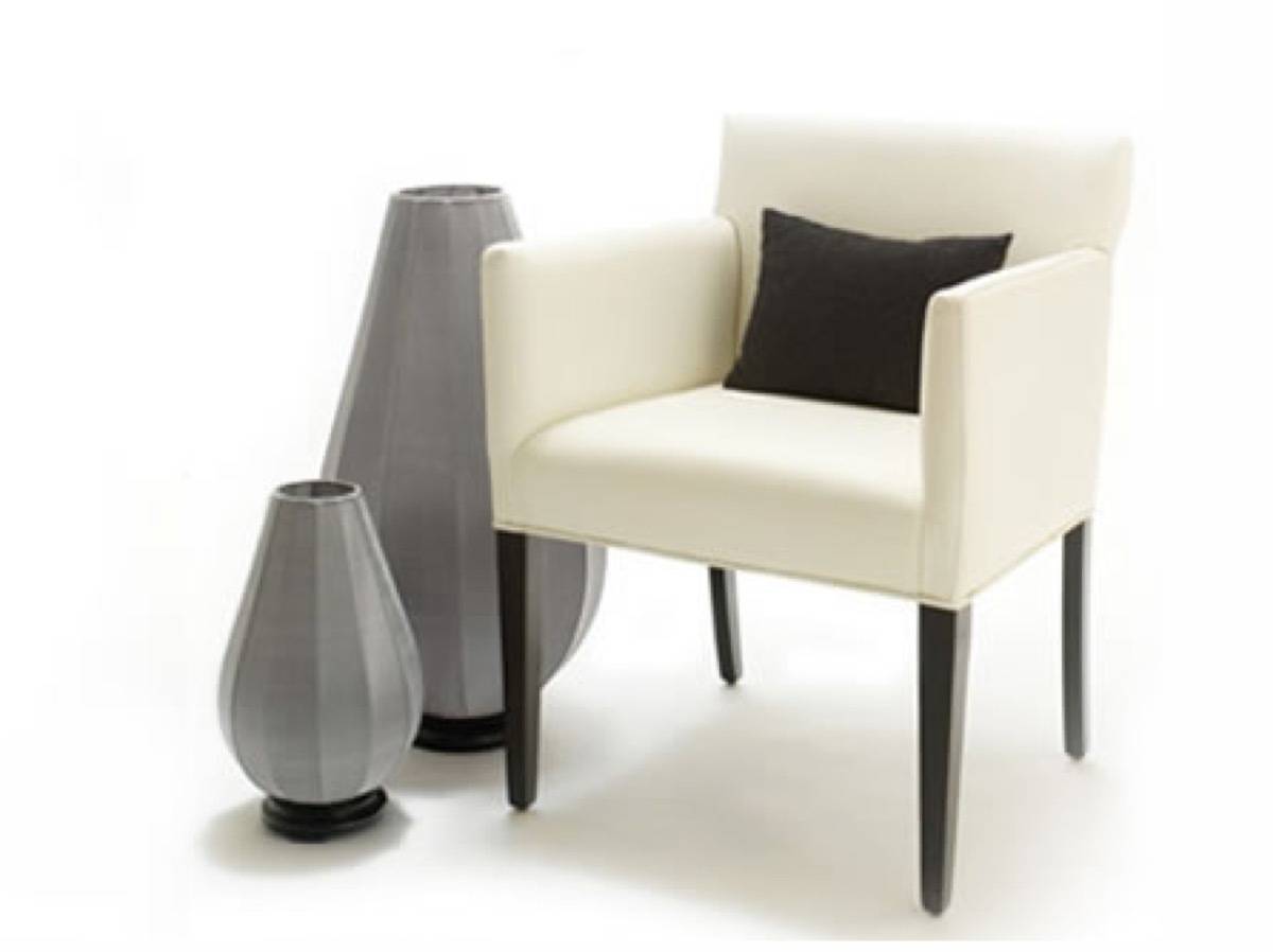 A white chair with a black cushion is sitting near two grey vases.