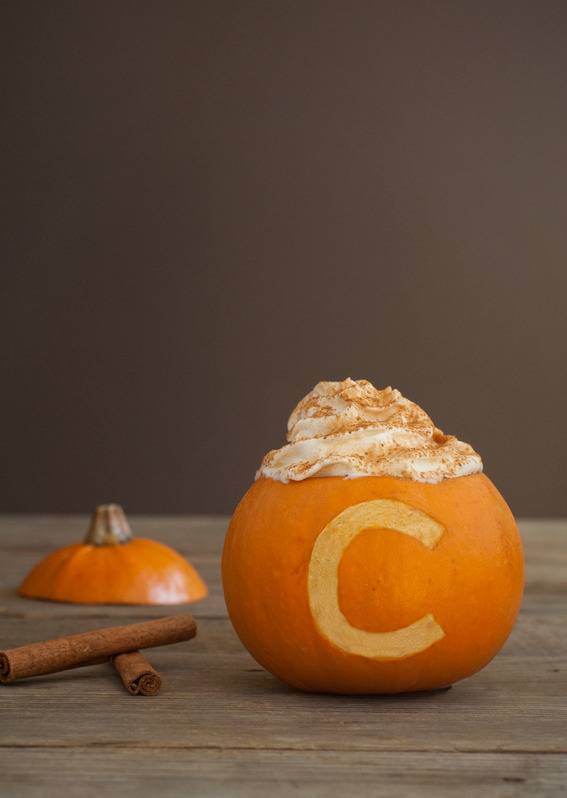 A C has been carved out of a pumpkin near cinnamon sticks.