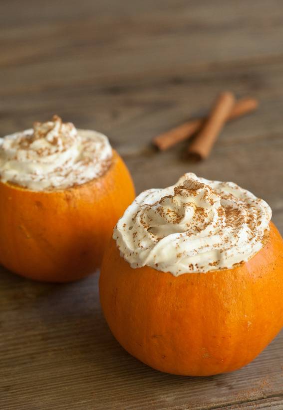 Pumpkins converted into mugs with foamy topping near cinnamon sticks.