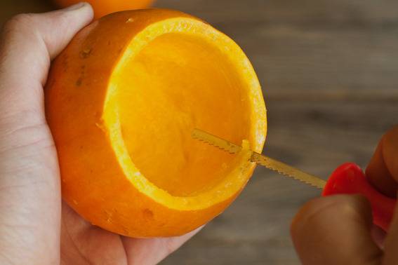 A person is using a tool to carve out a fruit.