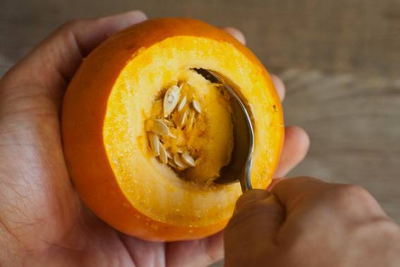 A person is using a spoon to scoop the seeds out of a yellow fruit.