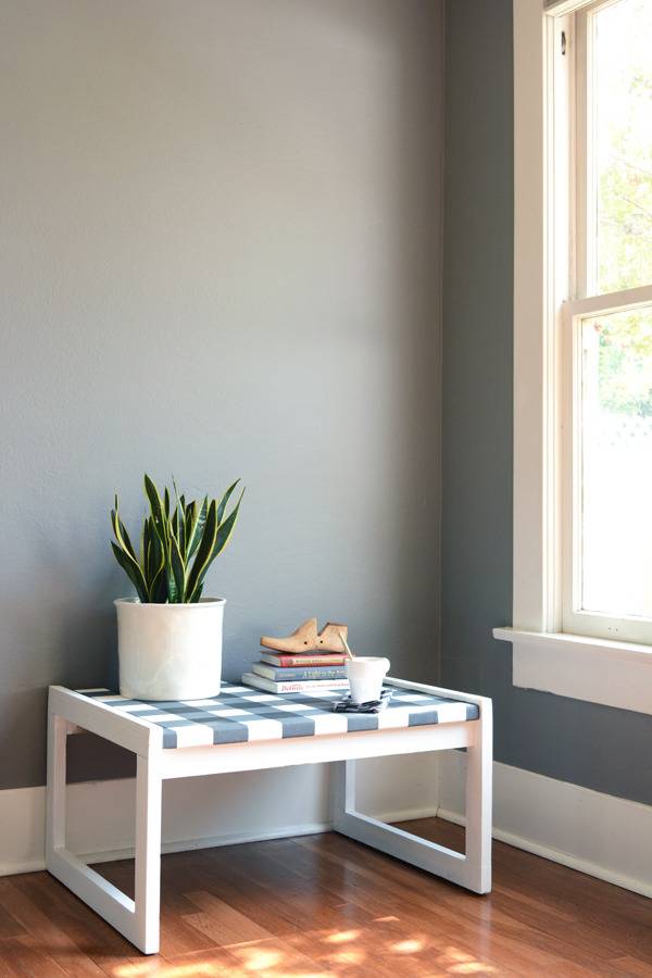 A table lying on the wooden floor in a corner of a room with a vase and books on top of it