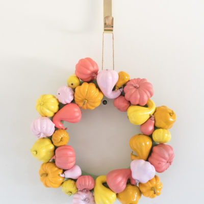 A wreath is made out of small pumpkins and gourds that have been painted yellow, orange and pink.