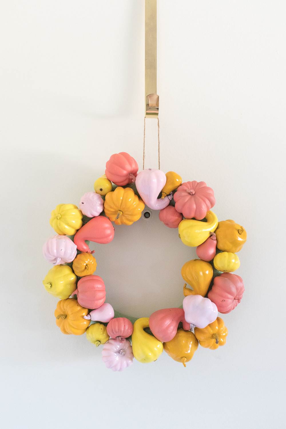 A wreath is made out of small pumpkins and gourds that have been painted yellow, orange and pink.