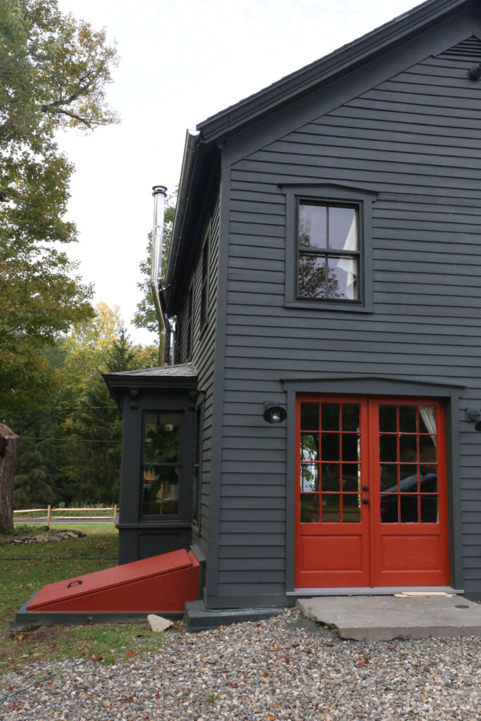 This home is painted a greenish-charcoal called Deep River and the door is Grand Canyon Red, both from Benjamin Moore. Image from Remodelista, At Home in Upstate, New York, with Amanda Pays and Corbin Bernsen.