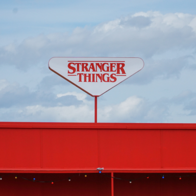 Red and white sign that says Stranger Things written above red building.