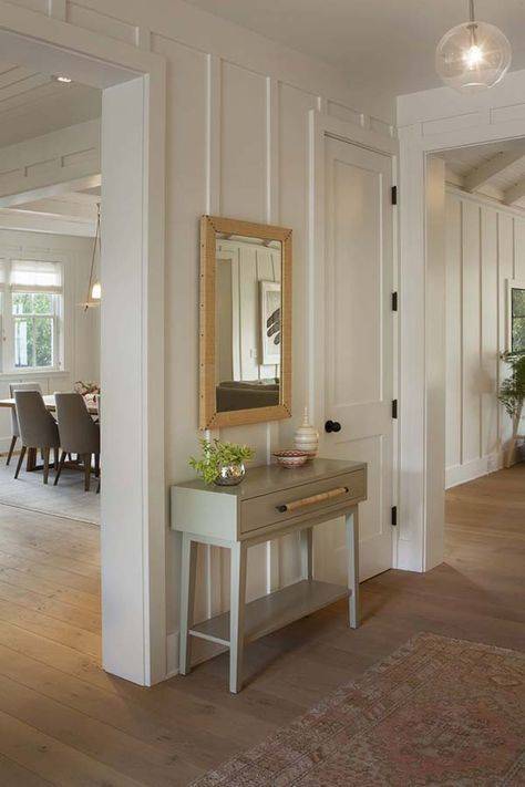 Vertical cream colored wainscoting panels with beige framed mirror and grey table.