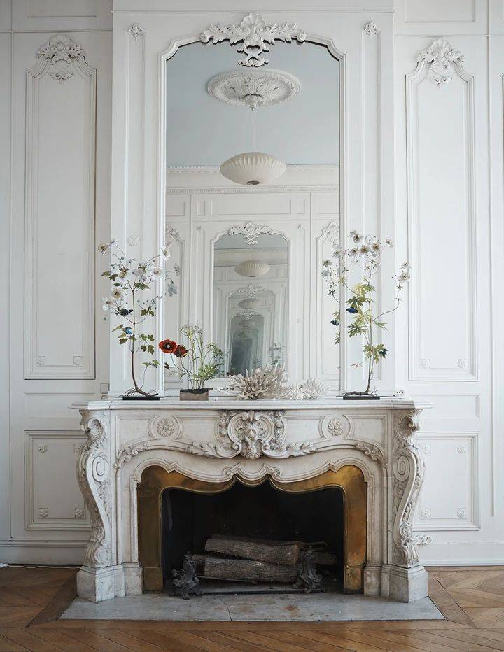 French style fireplace in white background of living room with two plants on mantle 