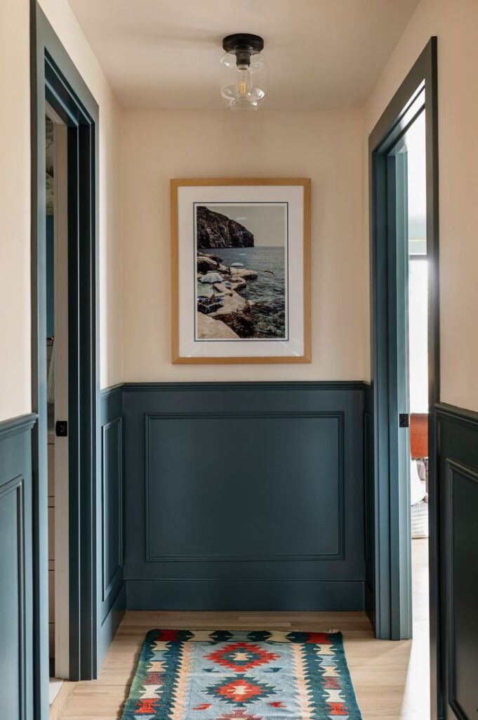 Greenish blue lower panel wainscoting in entryway with cream walls covered by framed art