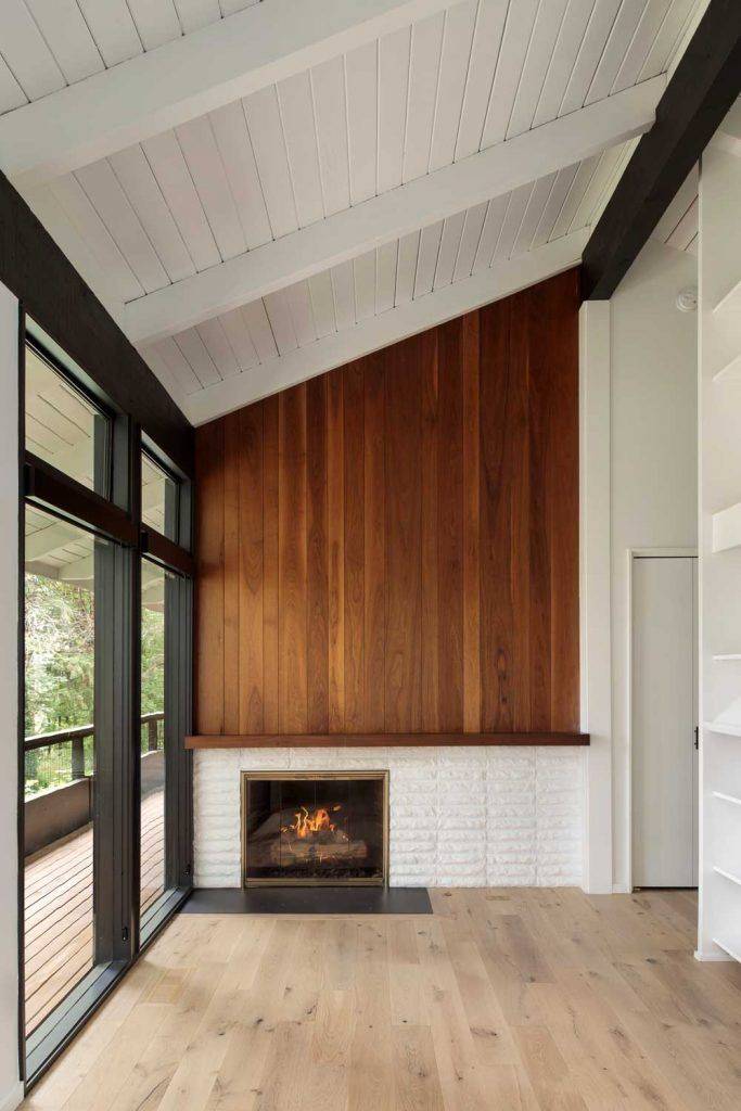 Mid-Century Modern fireplace in living room with tall walls, high black windows, wood and white walls in background