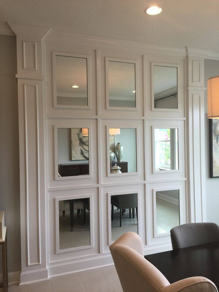 Mirrored wall with wainscoting panels behind dining room space with grey and cream chair