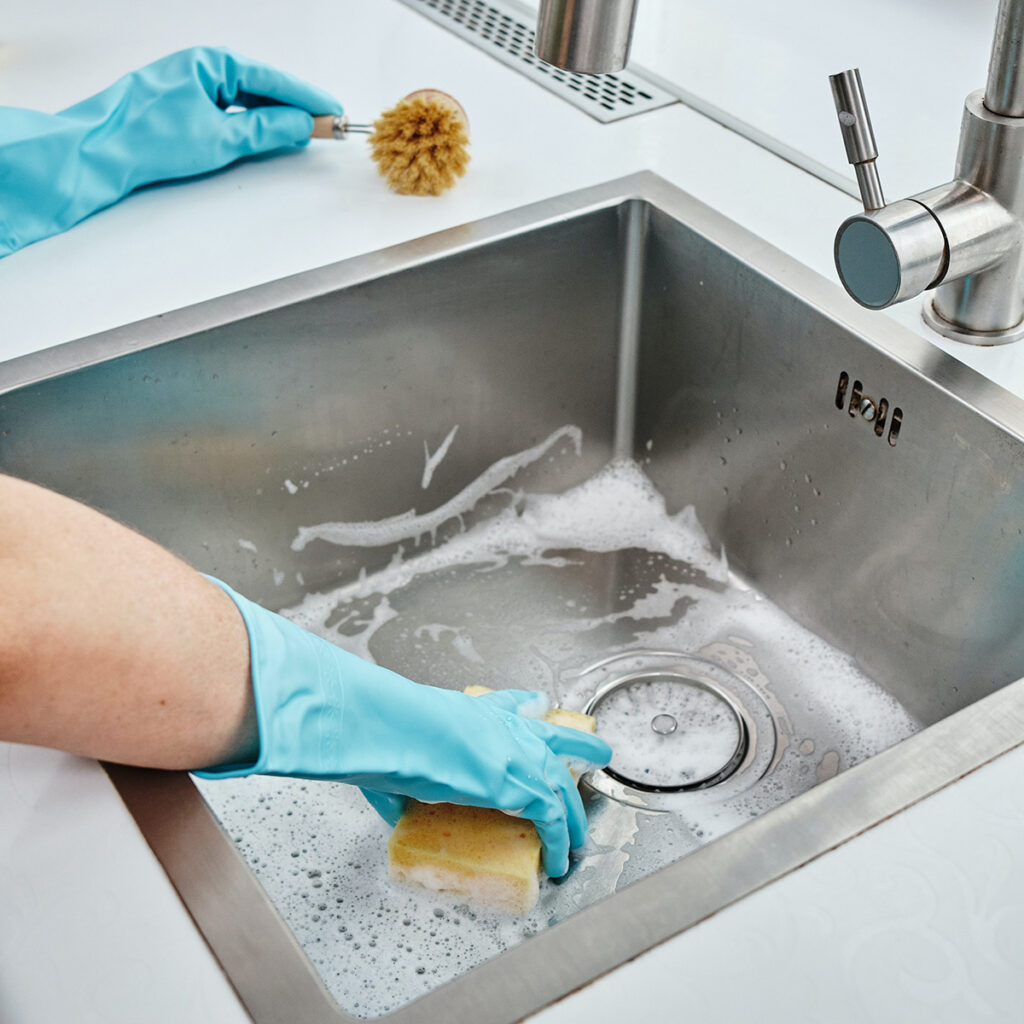 person cleaning a stainless steel sink with dish gloves.