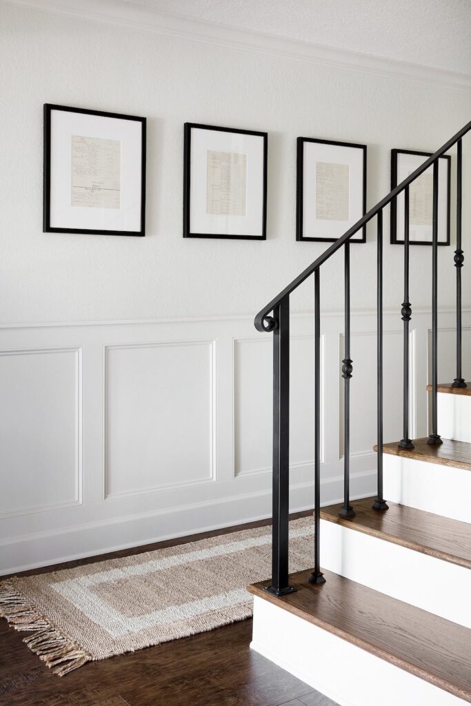 Modern Flat Panel Wainscoting against a white wall near stairs, wood flooring and black framed paintings.