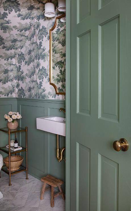 Sage green bathroom wainscoting with brass fixtures and wallpaper