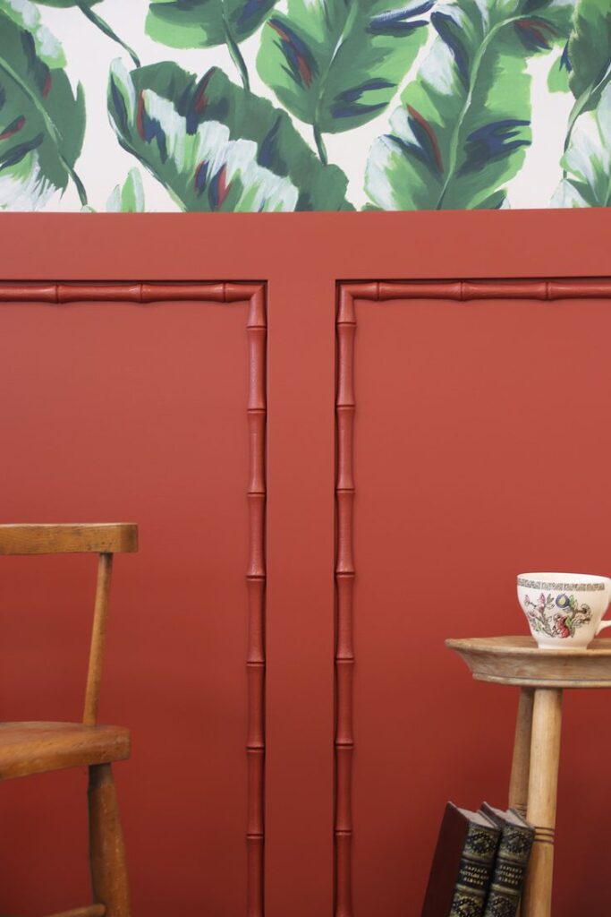 Red bamboo wainscoting on wall with green floral wallpaper