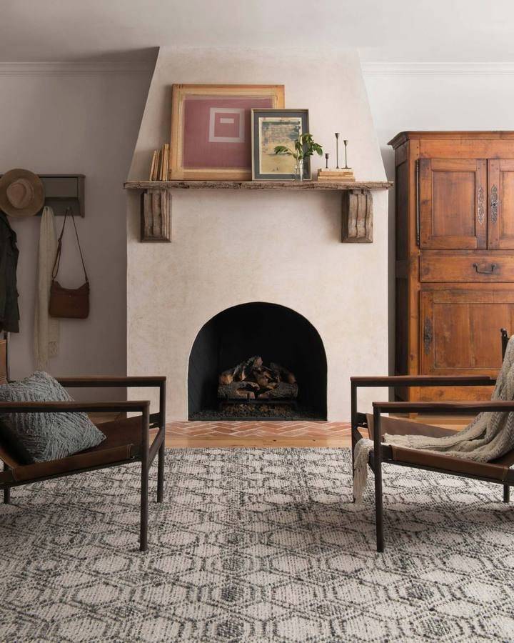 Living room with cream rustic fireplace, tile rug and brown armoire 