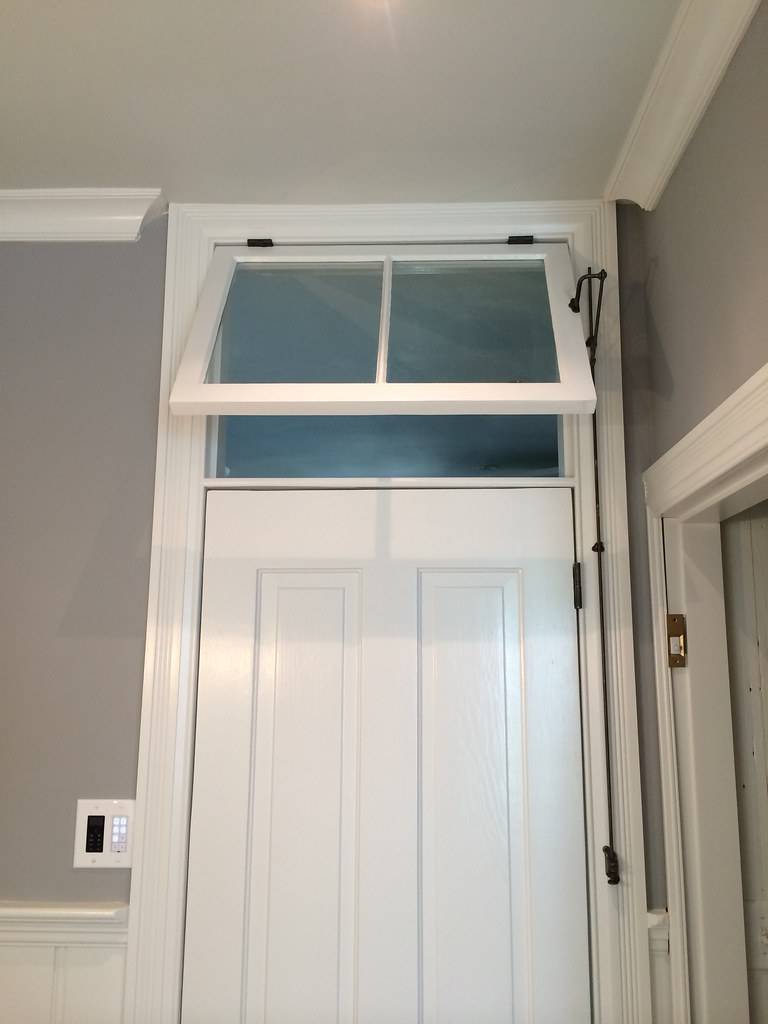 White transom window over entryway door with black brackets to help hold it open