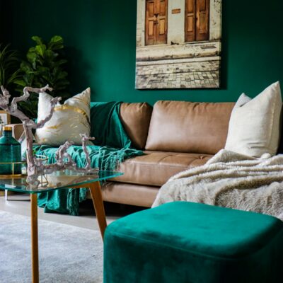 beige leather couch and green ottoman in dark emerald green painted walls
