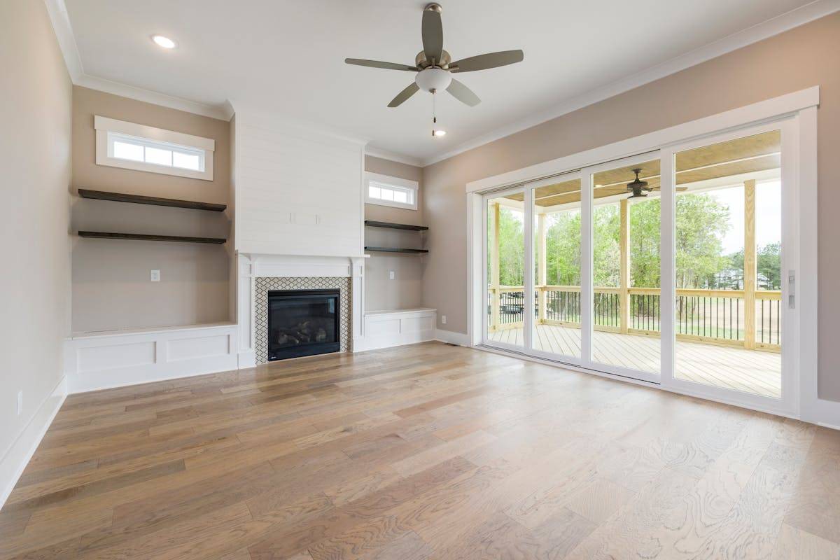Spacious living room with fireplace and ceiling fan overlooking veranda through glass doors.